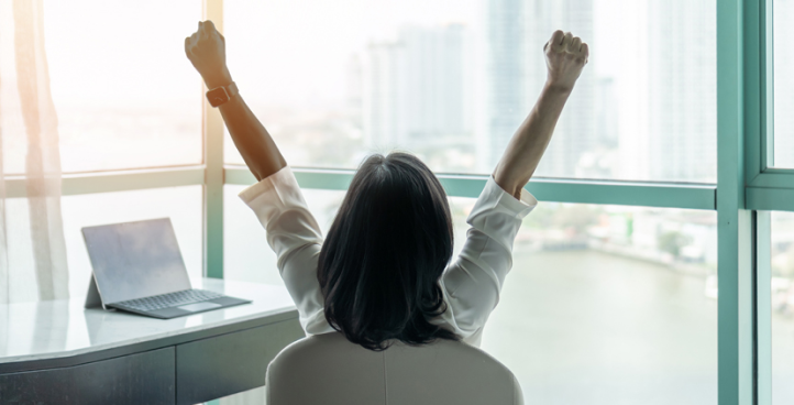 A woman sitting at a desk with a laptop stretches.