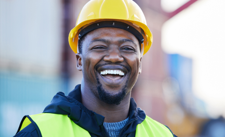 Smiling man wearing a construction hat and reflective vest.