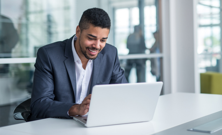 A young man in a suit sits at a table with a laptop.