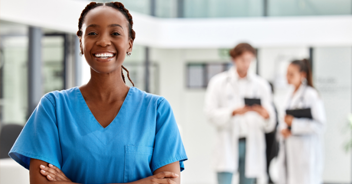 A young nurse in light blue scrubs smiles.